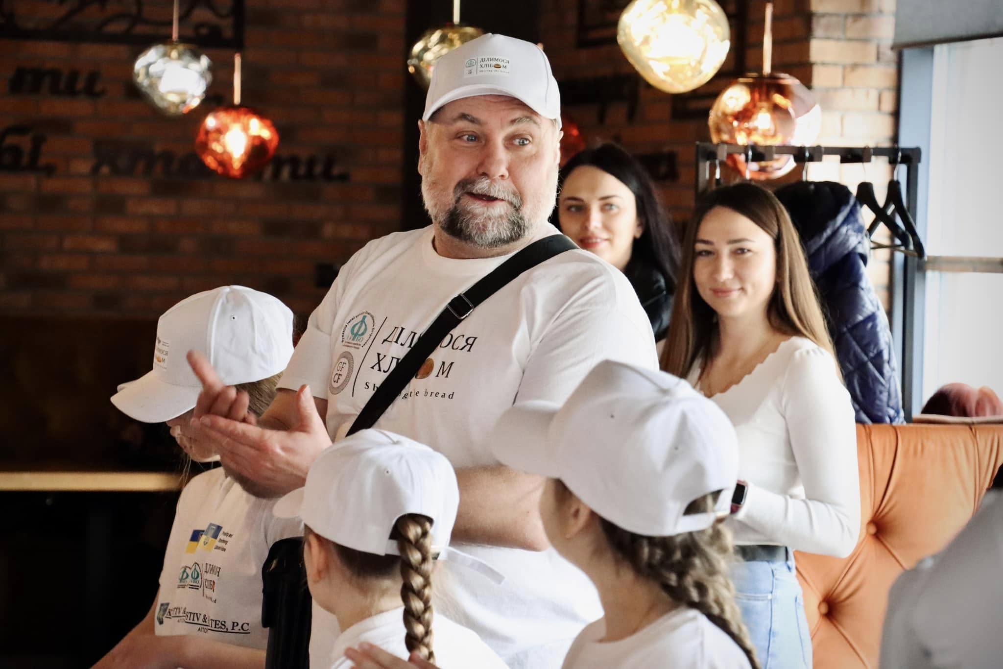 Чоловік у білій футболці розповідає щось дітям.